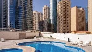 Una piscina con sillones de descanso, rodeada de edificios altos.
