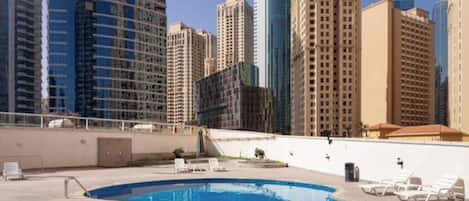 A swimming pool with lounge chairs, surrounded by high-rise buildings.