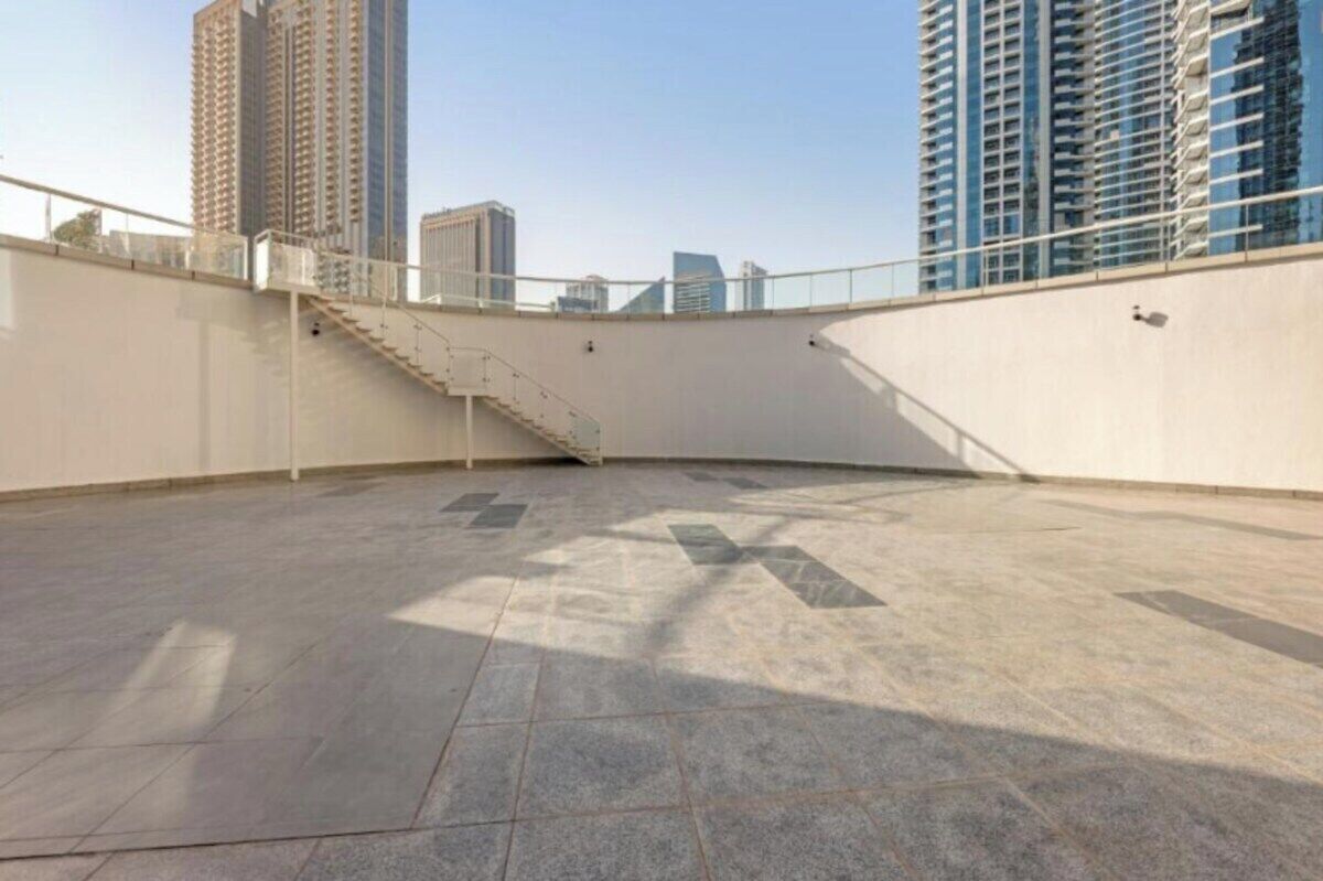 An empty rooftop terrace with a staircase leading to an upper level, surrounded by high-rise buildings.