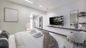 Habitación de hotel moderna con una cama grande, un televisor de pantalla plana, un espejo y un sofá.