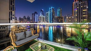 Un balcón con vistas a un horizonte urbano al anochecer, que muestra edificios modernos y una masa de agua.