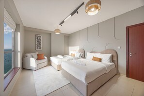 Ein modernes Hotelzimmer mit einem großen Bett, zwei Einzelbetten, einer Couch, einem Fenster mit Aussicht und einer Deckenleuchte.