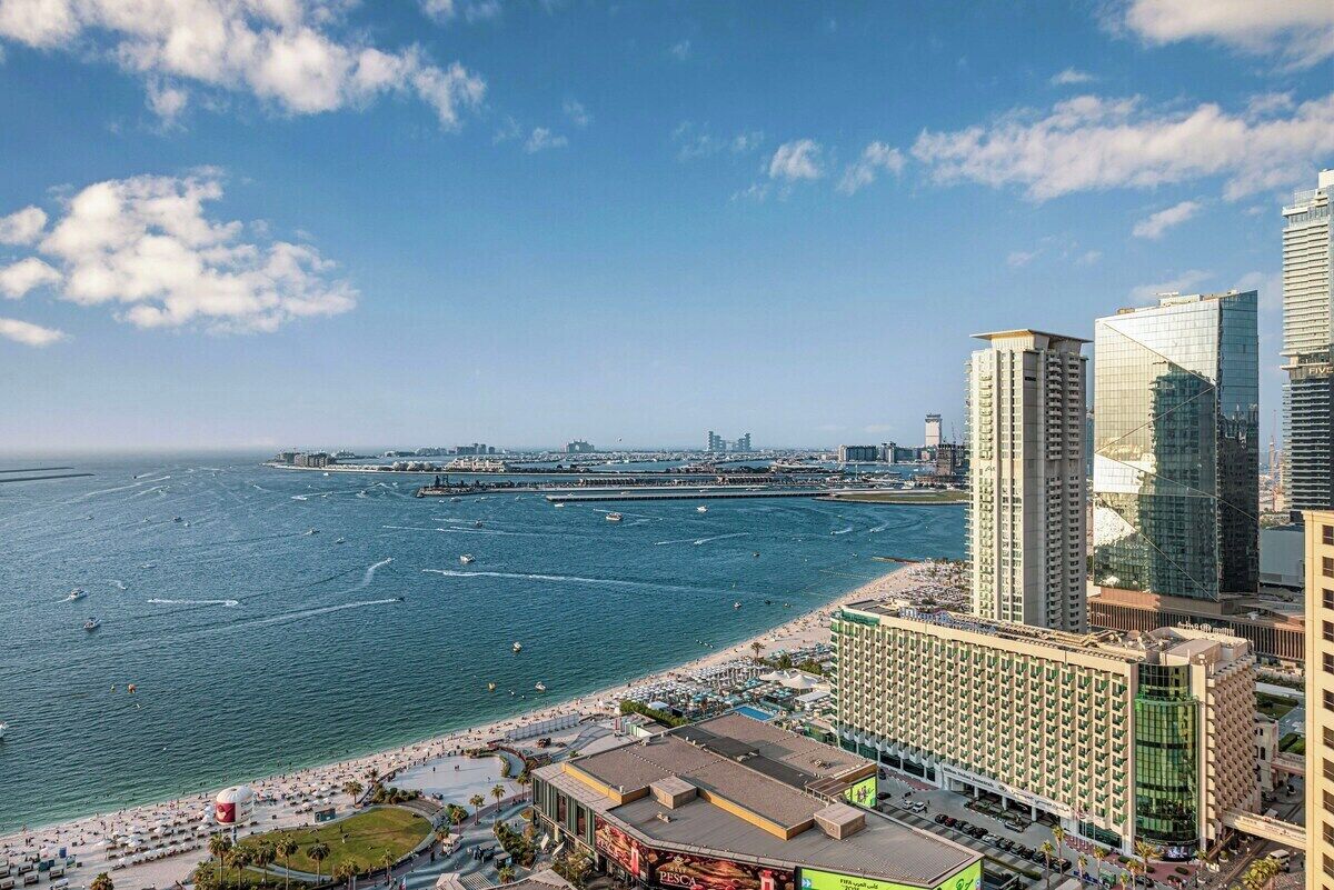 Un paisaje urbano costero con un hotel frente a la playa, un puerto deportivo y edificios altos.