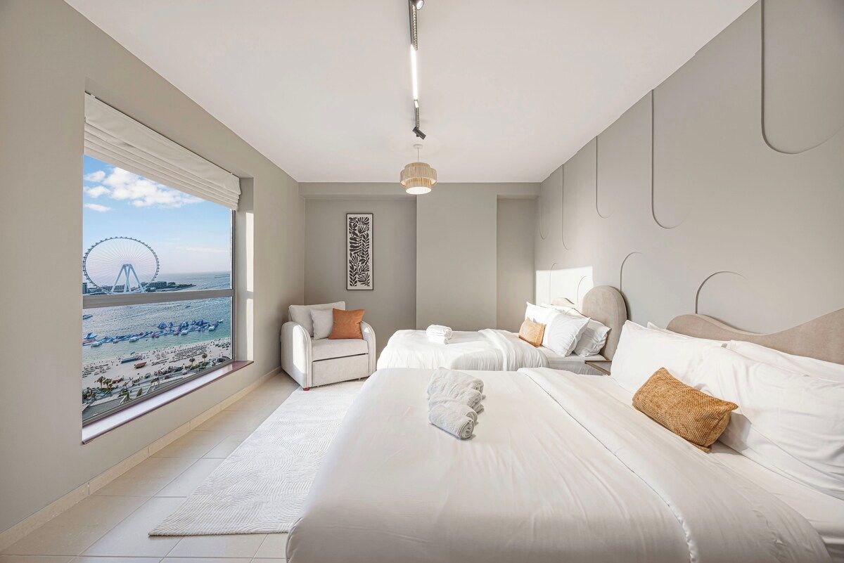 Ein Hotelzimmer mit großem Fenster, zwei Betten, einem Sessel und einer Pendelleuchte.