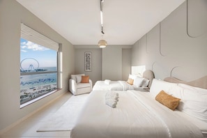 A hotel room with a large window, two beds, a chair, and a hanging light fixture. - JBR Walk / Ocean Views / Pool Table / Gym / Pool (Dubai)