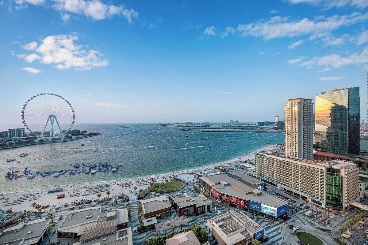Un paysage urbain côtier avec une grande roue bien visible, une plage et des immeubles modernes de grande hauteur.