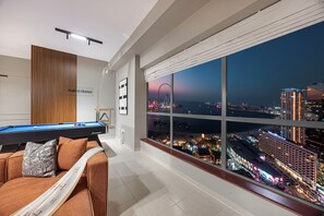 A modern living room with a pool table, a sofa with a throw blanket, and a large window offering a city view. - NYE Atlantis Fireworks Show| Palm Views|Pool Table (Dubai)