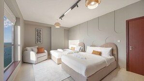 Ein modernes Schlafzimmer mit einem großen Bett, zwei Einzelbetten, einem Sofa und Meerblick.
