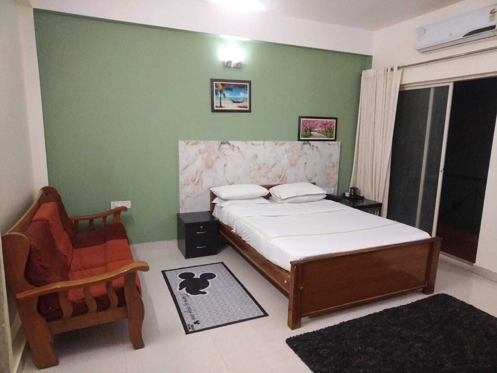 A bedroom with a bed, a nightstand, a chair, a picture on the wall, and a window with curtains.