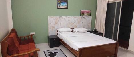 A bedroom with a bed, a nightstand, a chair, a picture on the wall, and a window with curtains.
