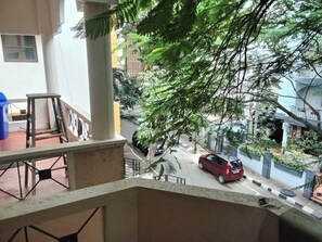 Un balcón con vistas a una calle, un coche rojo estacionado en la vía y un árbol con follaje verde.