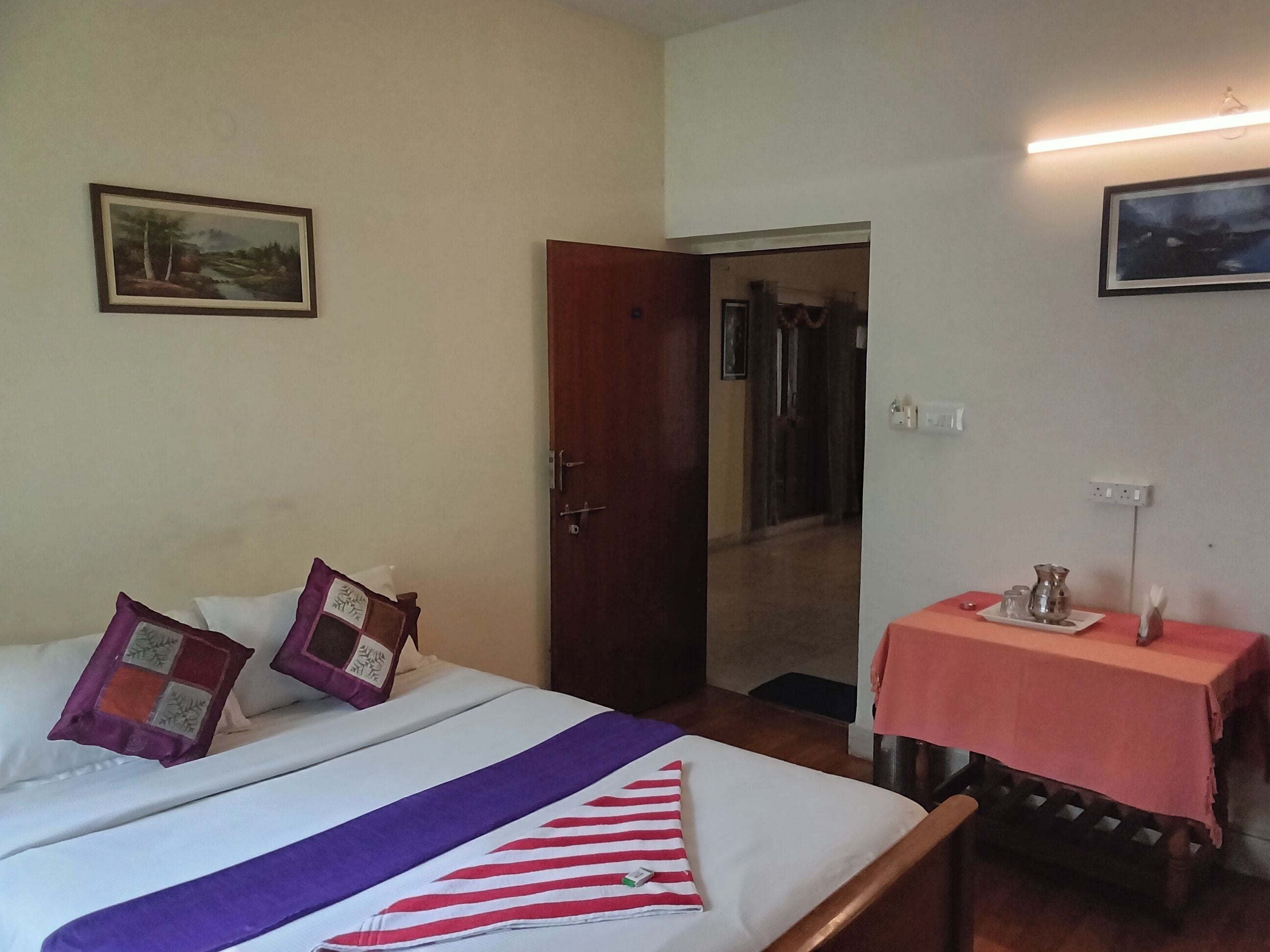 A hotel room with a bed, a small table with a pitcher, and a door leading to another room.