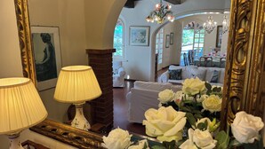 Quarto com um espelho grande e ornamentado, um sofá branco e um vaso de rosas brancas.