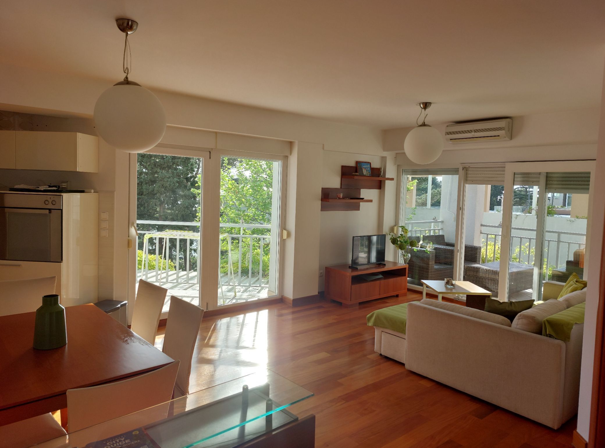 Una sala de estar moderna con comedor, un sofá, un televisor y un balcón con vista a la vegetación.