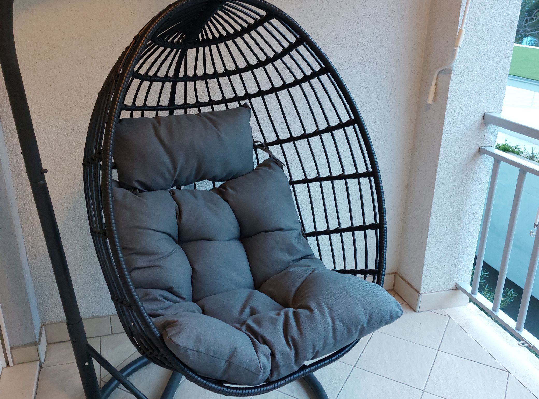 A black wicker chair with grey cushions on a balcony.