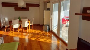 A modern living room with a wooden floor, a dining area with chairs, a table, and a large sliding glass door leading to an outdoor area. - Villa Nižić Makarska (Makarska)