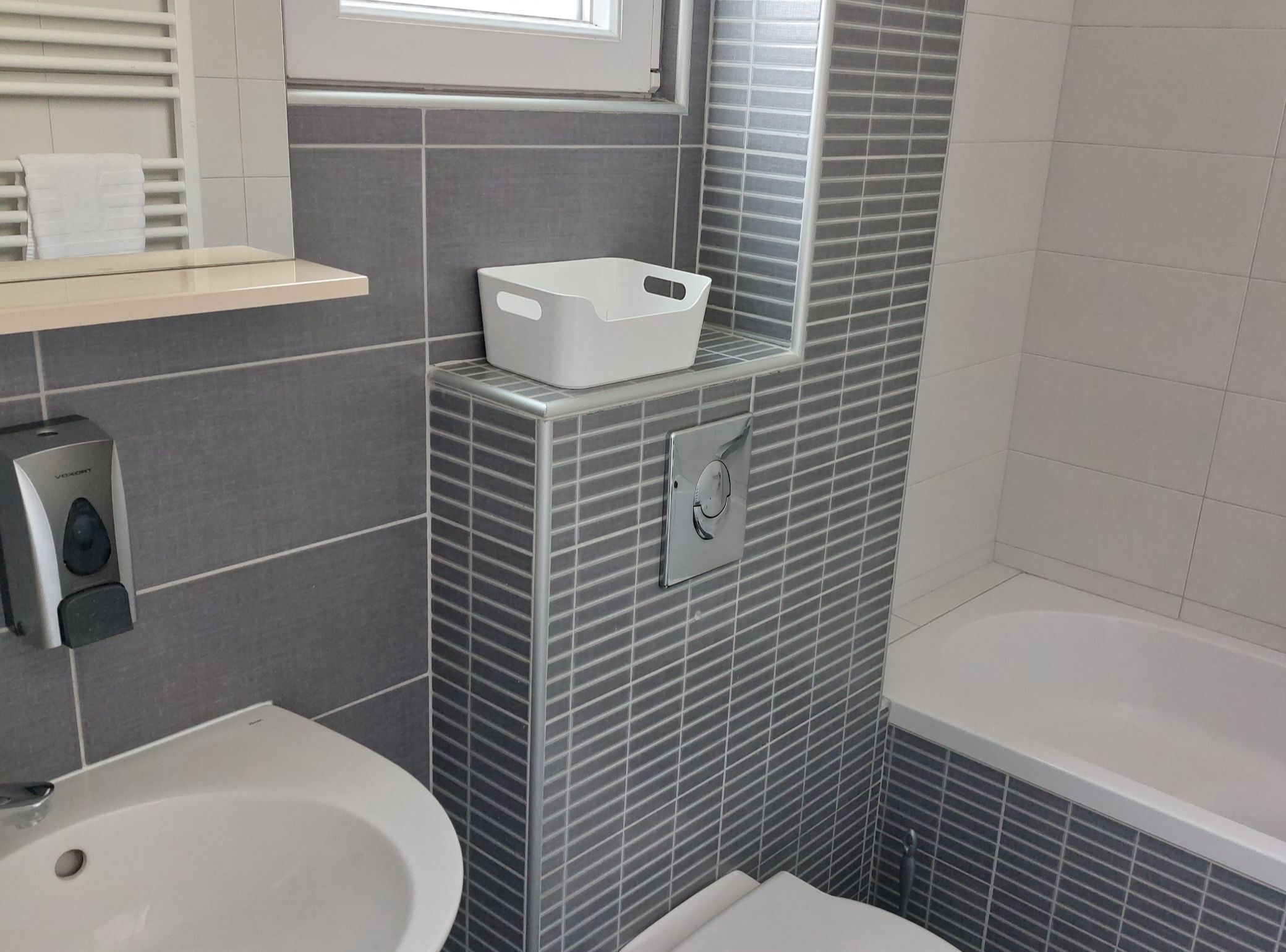 A bathroom with a white bathtub, a toilet, a bidet, and a towel rack.