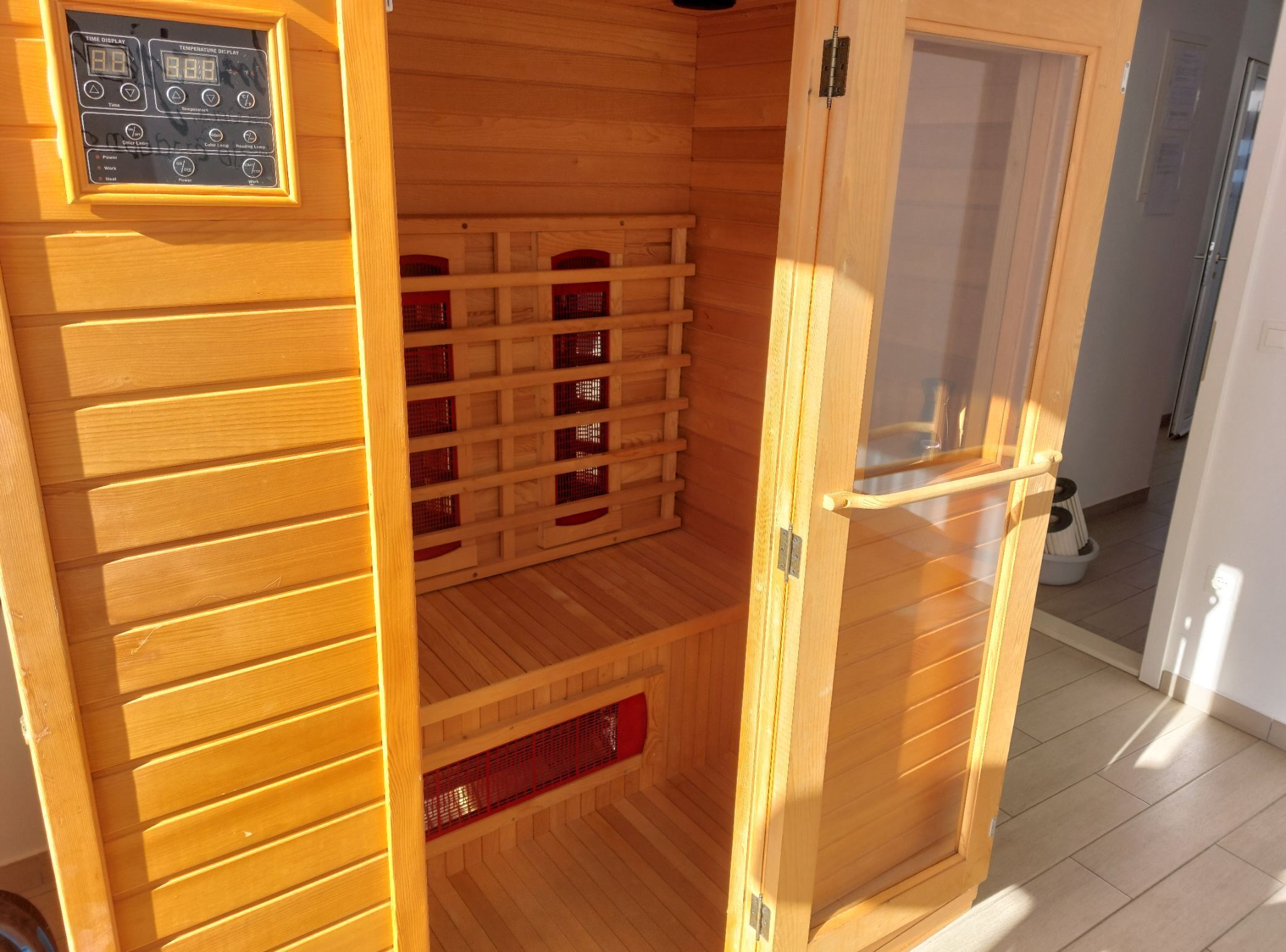 Una sauna amb parets de fusta, un panell de control i una porta de vidre.