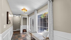 A hallway with a bench, a large window with curtains, and a door leading to another room. - Endless Family Entertainment, Fire Pit, 2 Kings! (Wichita)