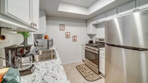 Una cocina moderna con electrodomésticos de acero inoxidable, armarios blancos y encimera de mármol.