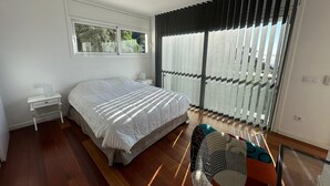 A modern bedroom with a large bed, a bedside table, a chair, and a view through floor-to-ceiling windows. - Beautiful Villa Martin AV-88 (Roses)