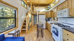 A compact kitchen with wooden cabinets, a stove, and a refrigerator. There is a window providing a view of the outdoors. - Private Hot Tub & Deck: Woodland Park Tiny Home! (Woodland Park)
