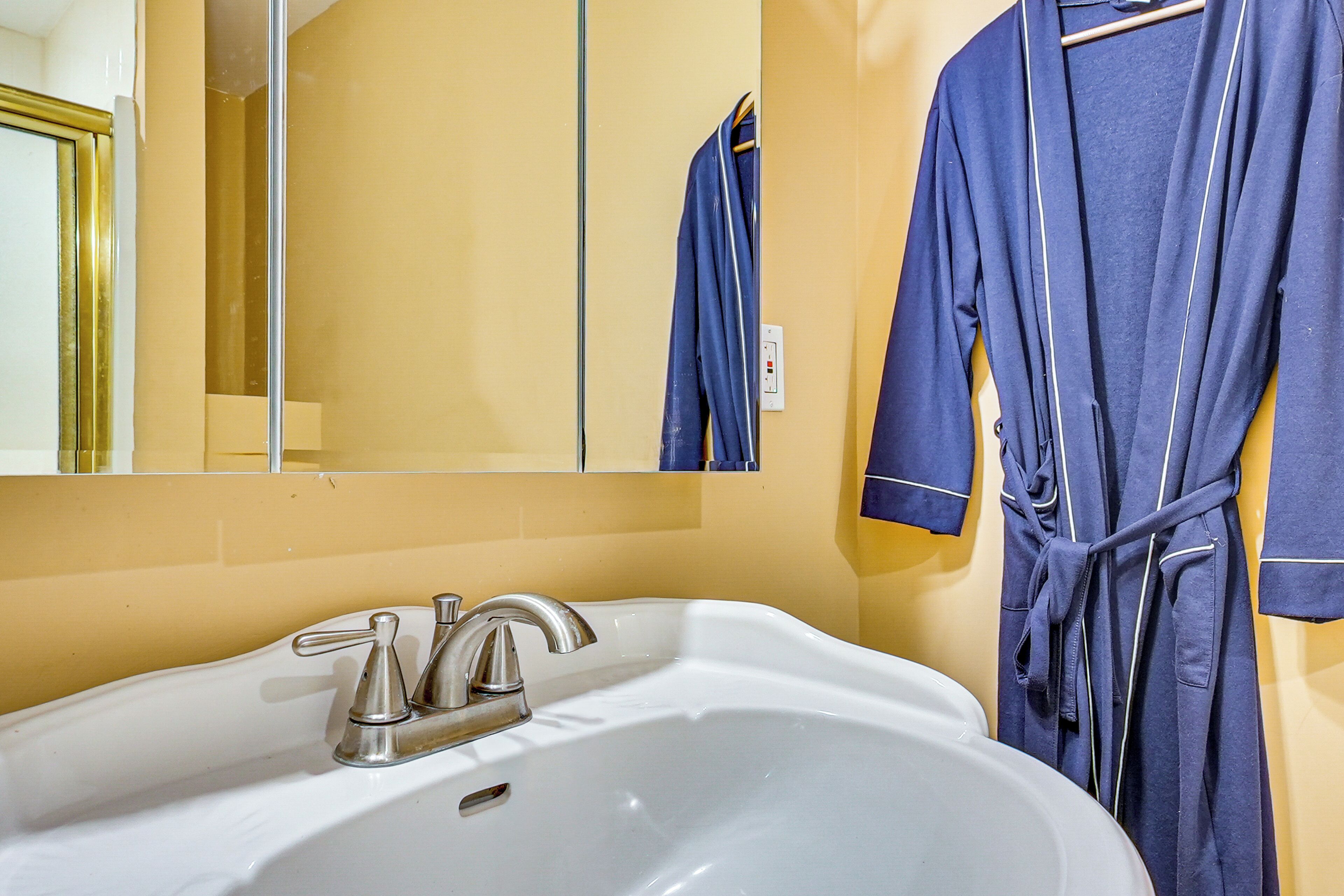 Un ba ño con un lavabo blanco, un espejo y una bata azul colgada en la pared.