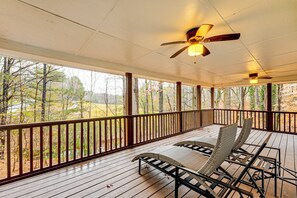 A covered porch with a ceiling fan, wooden railings, and a view of a wooded area.