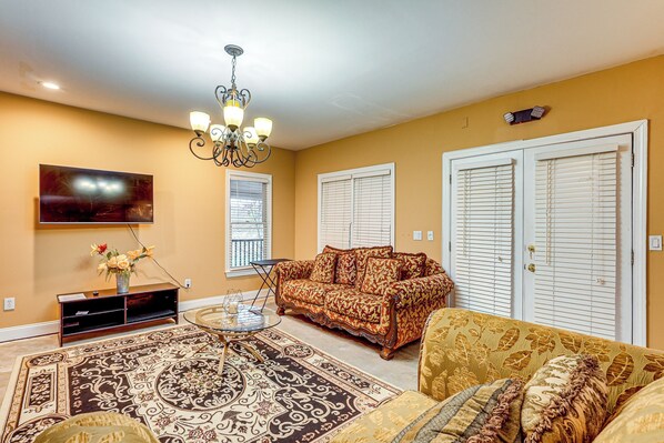A living room with a patterned rug, a sofa, a television, and a chandelier.