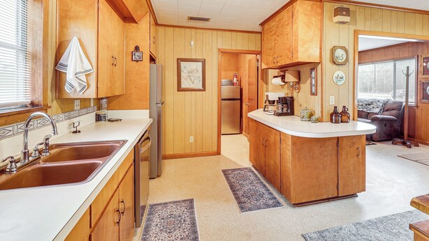 A kitchen with wooden cabinets, a sink, and a refrigerator. There is a dining area with a couch and a window.