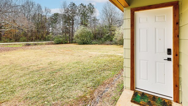 Une vue de face d’une maison avec une porte blanche, un petit porche et une cour couverte d’herbe.