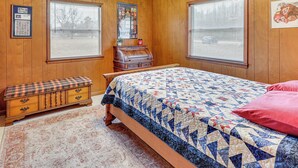 A bedroom with wooden walls, a bed with a quilt, a bench, and a dresser.