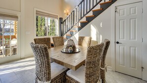 A dining area with a wooden table and wicker chairs, a staircase with black railings, and a white door.