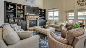 A spacious living room with a stone fireplace, comfortable seating, and large windows offering a view of the outdoors.