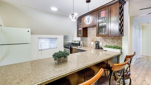 Una cocina con encimeras de granito, armarios de madera e iluminación colgante.