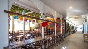 Ein Restaurant mit langen Gemeinschaftstischen und Stühlen, einer Holzbalkendecke und einer grünen Wand mit hängenden Dekorationen.