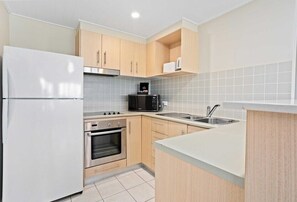 A compact kitchen with a refrigerator, microwave, oven, and sink. - The Pool Resort Kingscliff - One Bedroom (7114) (Kingscliff)