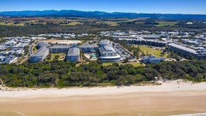Eine Luftaufnahme eines Küstenresorts mit mehreren Gebäuden, einem Sandstrand und Meereswellen.