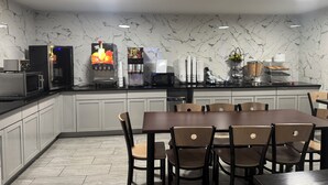 A modern kitchen with a marble backsplash, a fruit juice dispenser, a coffee machine, and a buffet setup.