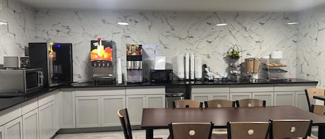 A modern kitchen with a marble backsplash, a fruit juice dispenser, a coffee machine, and a buffet setup.