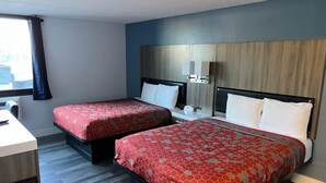 A hotel room with two beds, a desk, and a window with curtains.
