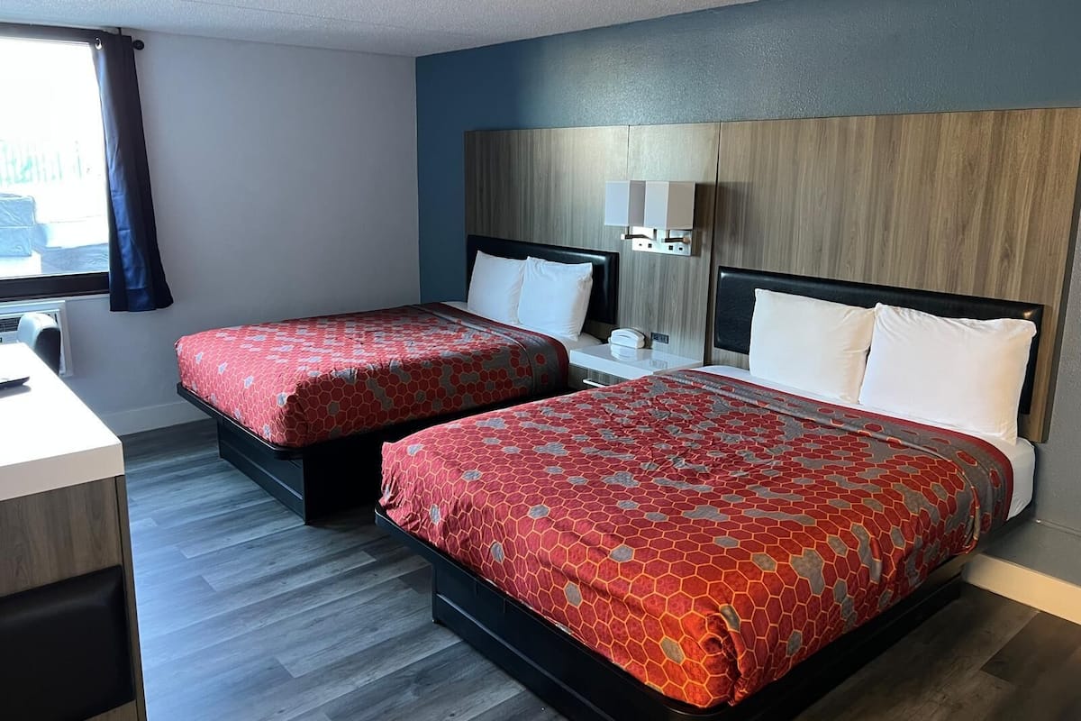 A hotel room with two beds, a desk, and a window with curtains.