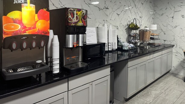 A modern kitchen area with a fruit juice dispenser, coffee machine, and various food containers.