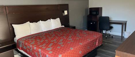 A hotel room with a large bed, a desk, a chair, and a TV.