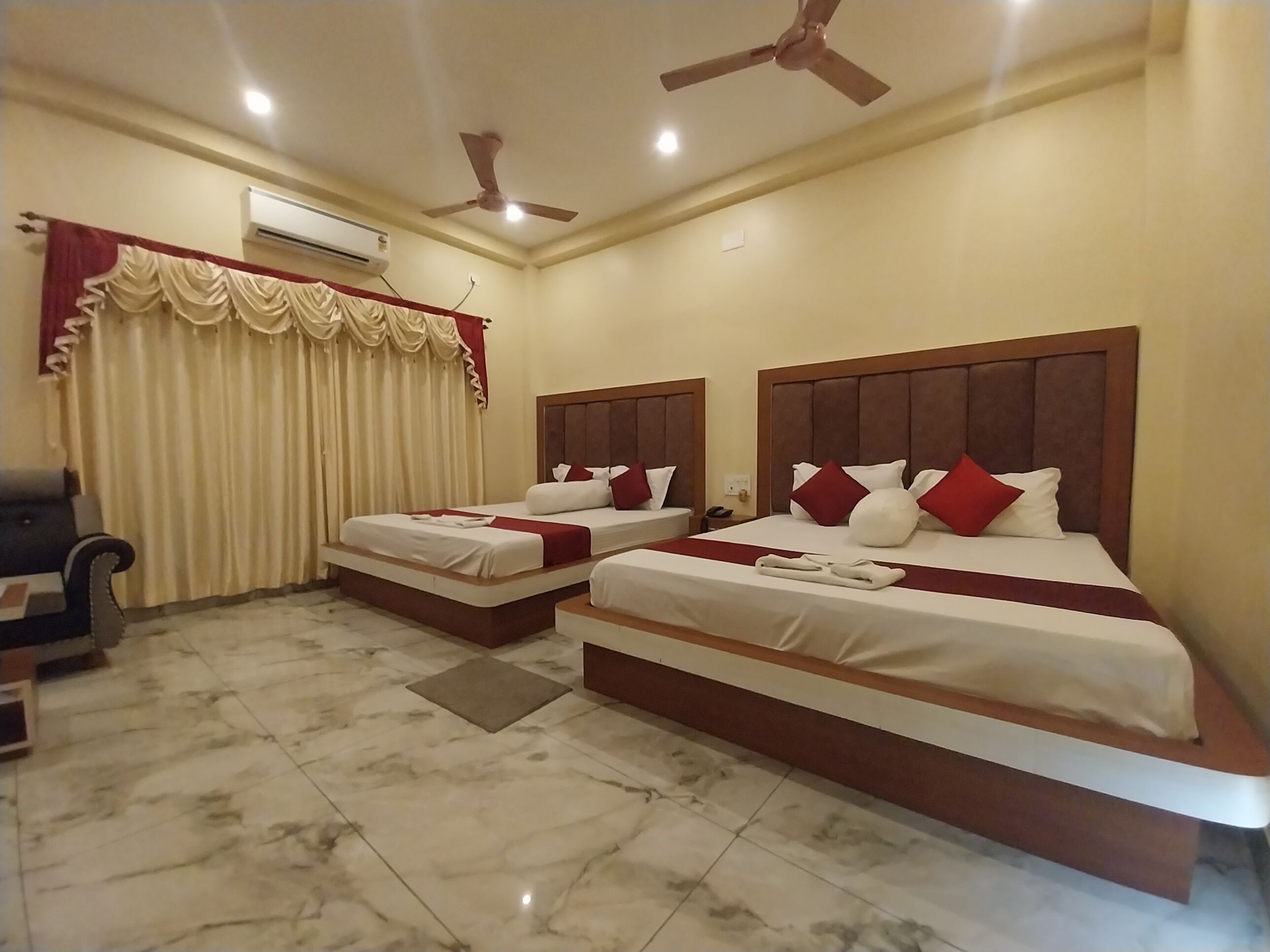 A hotel room with two beds, a ceiling fan, an air conditioning unit, and a marble-tiled floor.