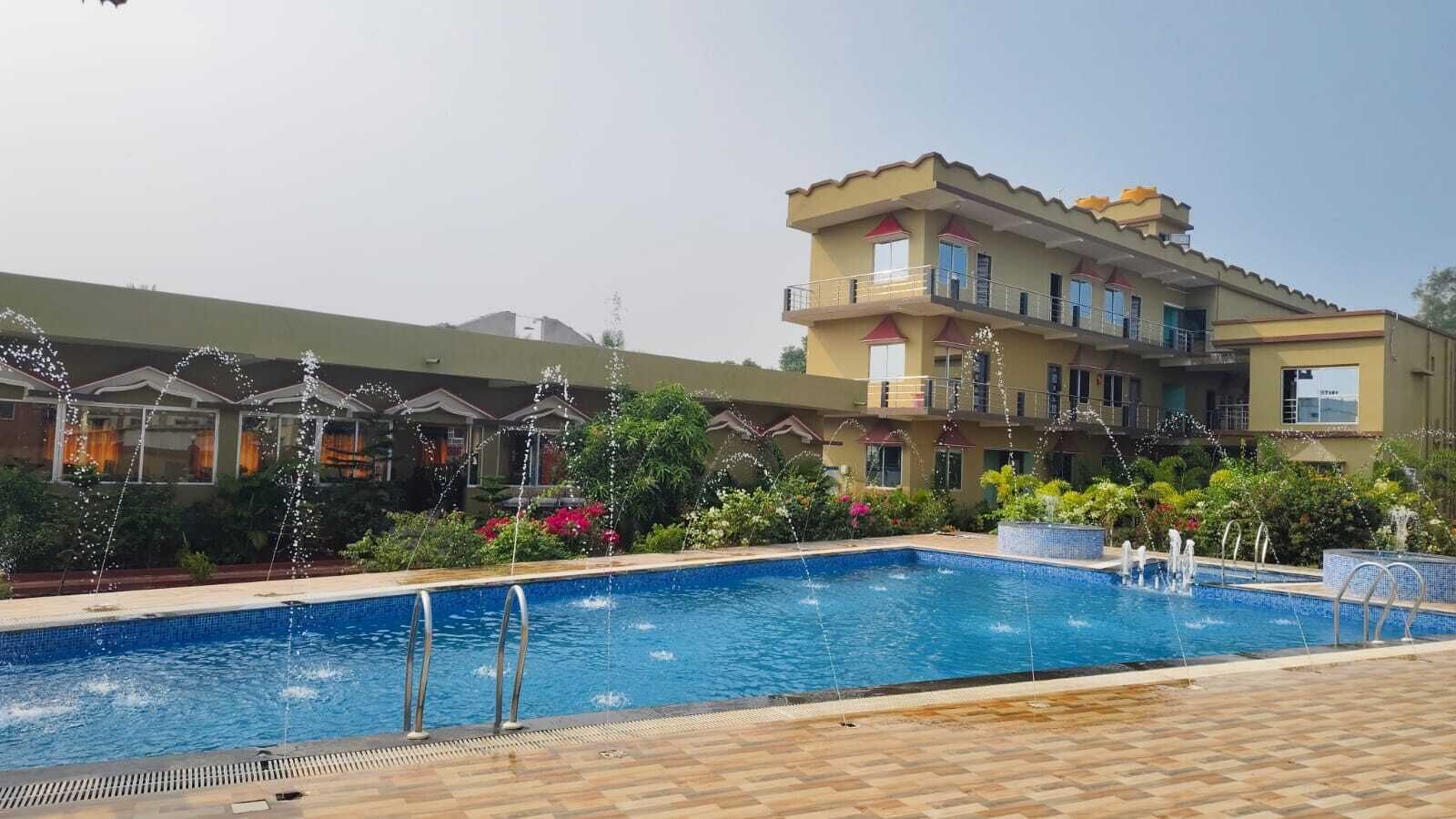A swimming pool with water fountains, surrounded by a wooden deck and a building with balconies.