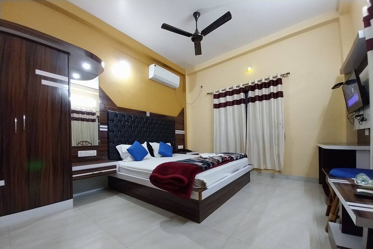 Un dormitorio con cama, armario, ventilador de techo, aire acondicionado, cortinas y televisor.