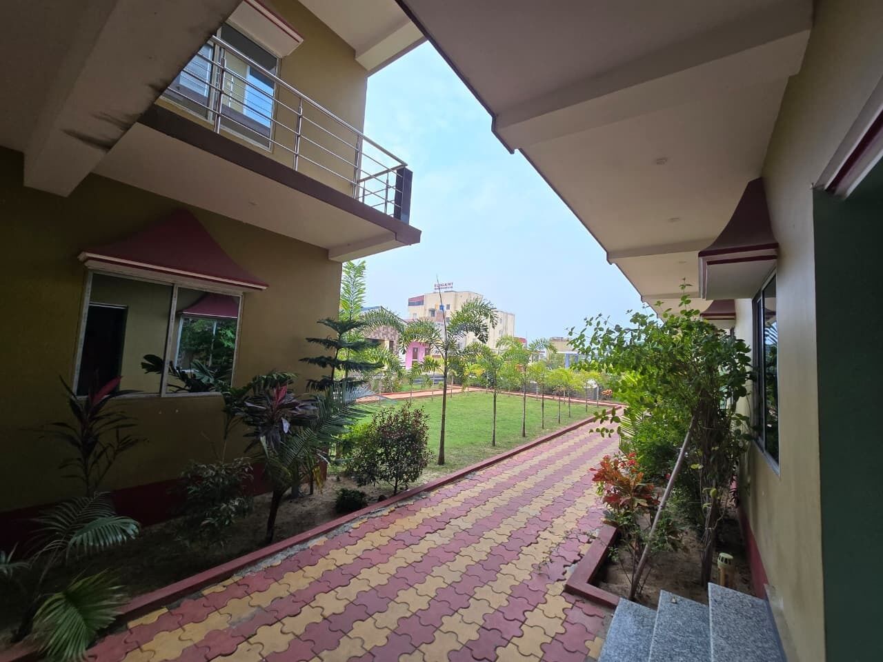 Un immeuble à plusieurs étages doté d’un balcon, d’un chemin pavé et d’une zone herbeuse avec des arbres.
