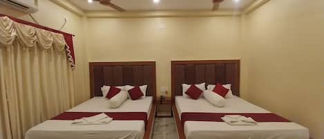 A hotel room with two beds, each with a wooden headboard and white bedding. There are ceiling fans and an air conditioning unit.