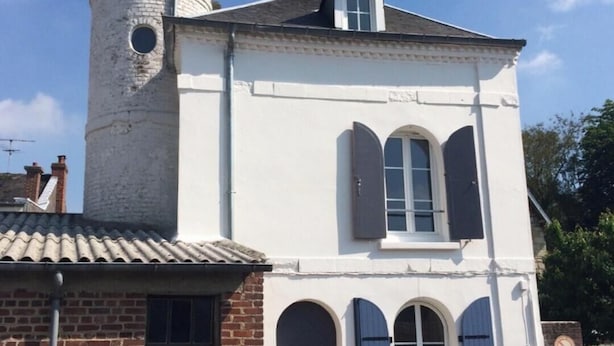 En bygning i to etager med en hvid facade, et lille tårn og et vindue med stormskodder.